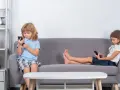Dzieci na kanapie, każde pochłonięte telefonem. Czy to znak, że od ilu lat dziecko może zostać samo w domu?