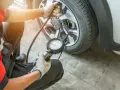 Controllo pressione gomme: il manometro indica pressione gomme troppo alta. Un meccanico con guanti sta verificando la pressione di un pneumatico.