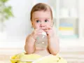 Ein süßes Baby mit blauen Augen hält eine Flasche und trinkt. Es scheint, als ob dieses Baby zu viel trinkt, aber es genießt jeden Schluck.