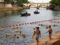 Gente nadando en el Sena de París, con boyas naranjas y una lancha de policía.