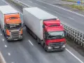 Dwa ciężkie tiry na autostradzie. Czerwony i pomarańczowy, każdy z dużą naczepą. Maksymalny nacisk na oś naczepy to klucz do bezpiecznego transportu.