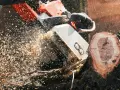 Praca z piłą spalinową czy elektryczną? Wióry lecą w powietrzu podczas cięcia drewna.