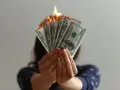 Hands hold burning US dollar bills, a visual metaphor for a use it or lose it budget.