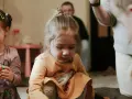 Skupiona dziewczynka w pomarańczowej bluzce, jak bawi się dziecko z autyzmem, z uwagą przygląda się swoim dłoniom.