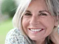 Mujer sonriente con cabello rubio y arrugas normales a los 50 años, disfrutando de un día al aire libre.