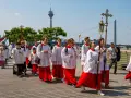 Jugendliche in Soutanen und Alba nehmen an einer Prozession teil, die an christliche Feiertage erinnert. Sie tragen Kreuze und Fahnen.