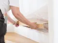 Person i arbetskläder lägger en ny trätrappa, ett steg i renovera trappa-projektet. Lim appliceras på trappstegens kanter.