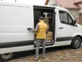 Kurier otwiera drzwi białego busa dostawczego, w którym widać paczki. Zastanawiasz się, ile waży bus dostawczy?