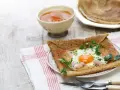 Crêpe de sarrasin garnie d'un œuf au plat, de jambon et d'herbes fraîches, servie avec une compote.