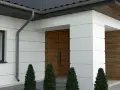 Nowoczesny dom z białym boniowaniem, drewnianymi drzwiami i ozdobnymi żywotnikami.