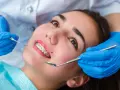 Młoda kobieta z aparatem ortodontycznym na zębach podczas wizyty u ortodonty. Dentysta w niebieskich rękawiczkach bada jej uśmiech.