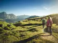 Persone in un percorso di trekking e hiking tra le montagne, con zaini e bastoncini da passeggio, sotto un cielo azzurro.