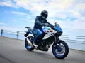 Motocyklista na niebiesko-białym Suzuki SV650X, idealnym motocyklu do 35kW, jedzie wzdłuż wybrzeża.