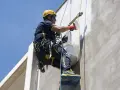 Trabajador en altura realiza instalación SATE, aplicando revestimiento en fachada con equipo de seguridad.