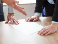 Dyskusja nad dokumentem, czy można odstąpić od umowy kupna samochodu. Dwie osoby pochylają się nad papierem na drewnianym stole.