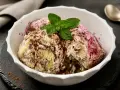 Schüssel mit Zuppa Inglese Gelato, garniert mit Minze und Schokoladenraspeln. Ein Löffel liegt daneben.