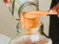 Une main dépose délicatement un scoby maison dans un bocal rempli de liquide pétillant.