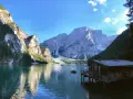 Malownicze jezioro w Dolomitach, z górami w tle i drewnianym domkiem na wodzie. Idealne miejsce na camping i podziwianie natury.