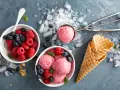 Himbeeren und Blaubeeren neben Schalen mit leckerem Milcheis selber machen. Eiswaffeln und ein Eisportionierer liegen bereit.