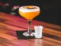 Orzeźwiający passion fruit martini z pianką i plasterkiem owocu, obok kieliszek wody gazowanej. Idealny na letnie wieczory.