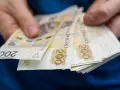 Dłonie trzymają stos banknotów 200 zł. Pieniądze mogą posłużyć do zapłaty czynszu administracyjnego.