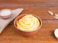 Una ciotola piena di soffice crema al burro, con zucchero in due piccole ciotole e decorazioni di erba secca su un tavolo di legno.