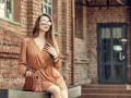 Elegancka kobieta w brązowej sukience i okularach przeciwsłonecznych, z torebką. Idealne buty do brązowej sukienki podkreślają jej styl.