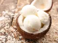Cremiges Kokosnuss Eis in einer halbierten Kokosnuss, umgeben von Kokosraspeln auf Holz. Ein tropischer Genuss!
