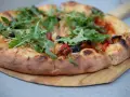 Idealne ciasto na pizzę z rukolą, oliwkami i papryką, wypieczone na drewnianej desce.