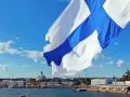 Flaga z niebieskim krzyżem powiewa nad portem w Helsinkach. W tle widać katedrę i inne budynki.