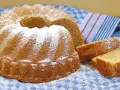 Puszysta babka z cukrem pudrem, obok niej kromki ciasta, na niebieskim ręczniku.