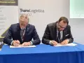 Dwóch mężczyzn w garniturach podpisuje dokumenty. Obok baner z napisem TransLogistica Poland, sugerujący umowę w branży gpw logistics.