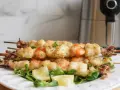 Spiedini di gamberi e calamari impanati, cotti alla perfezione nella friggitrice ad aria, serviti su un letto di insalata con spicchi di limone.