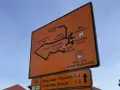 Pomarańczowa tablica z mapą szlaków rowerowych Velo Przemsza. Wskazuje drogę do Pustyni Błędowskiej, Czubatki Klucze i innych miejsc.