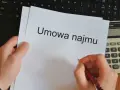 Ręka pisze długopisem na umowie najmu, obok kalkulator i laptop. Czas pomyśleć o podatku od najmu.