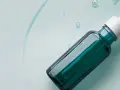 Szklana buteleczka z pipetką, wypełniona zielonym serum, na tle płynu z bąbelkami.