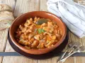 Guiso casero de oreja de cerdo en salsa de tomate, servido en cazuela de barro, acompañado de pan rústico y tenedores.