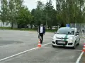 Młody mężczyzna ustawia pachołek na placu manewrowym. Biały Fiat Panda z literą "L" na dachu czeka na swój egzamin praktyczny kat b.