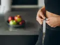 Kobieta mierzy talię centymetrem. Na blacie leżą jabłka. Zastanawiasz się, dlaczego waga stoi w miejscu?