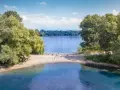 Sommerliche Idylle am Strandbad Wedau: Menschen genießen den Tag am Seeufer, einige radeln, andere entspannen im Sand.
