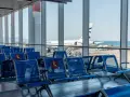 Puste niebieskie fotele na lotnisku we Włoszech, z widokiem na samolot Aegean i morze.