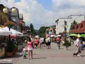 Tętniąca życiem ulica w Wiśle, pełna ludzi spacerujących, rowerzystów i psów. Wiele kawiarni i restauracji oferuje swoje atrakcje.
