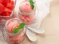 Erfrischendes Wassermelonen-Eis in Gläsern, garniert mit Minze. Daneben ein Schälchen mit frischen Wassermelonenstücken.