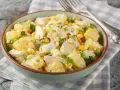 Una ciotola piena di insalata di pollo e patate, con mais, uova sode e cipollotto fresco.