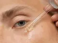 Nahaufnahme eines Auges, auf das ein Tropfen Öl aus einer Pipette aufgetragen wird.