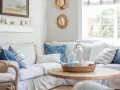 Un accogliente soggiorno con arredamento coastal: divano bianco, cuscini blu e bianchi, tavolino in legno e decorazioni marine.
