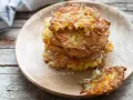 Una pila di dorate frittelle di patate, croccanti fuori e morbide dentro, servite su un piatto di legno.