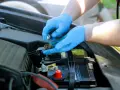 Mani con guanti blu puliscono i contatti arrugginiti della batteria rosso e nero dell'auto.