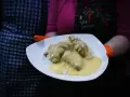 Porcja potrawki z kurczaka w kremowym sosie, podana na ryżu. Danie prezentowane na białym talerzu, trzymanym przez osobę w pomarańczowych rękawiczkach.