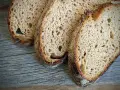 Drei Scheiben rustikales Sauerteigbrot liegen auf Holz. Der Sauerteig ist zu sauer, aber die Kruste ist perfekt gebräunt.